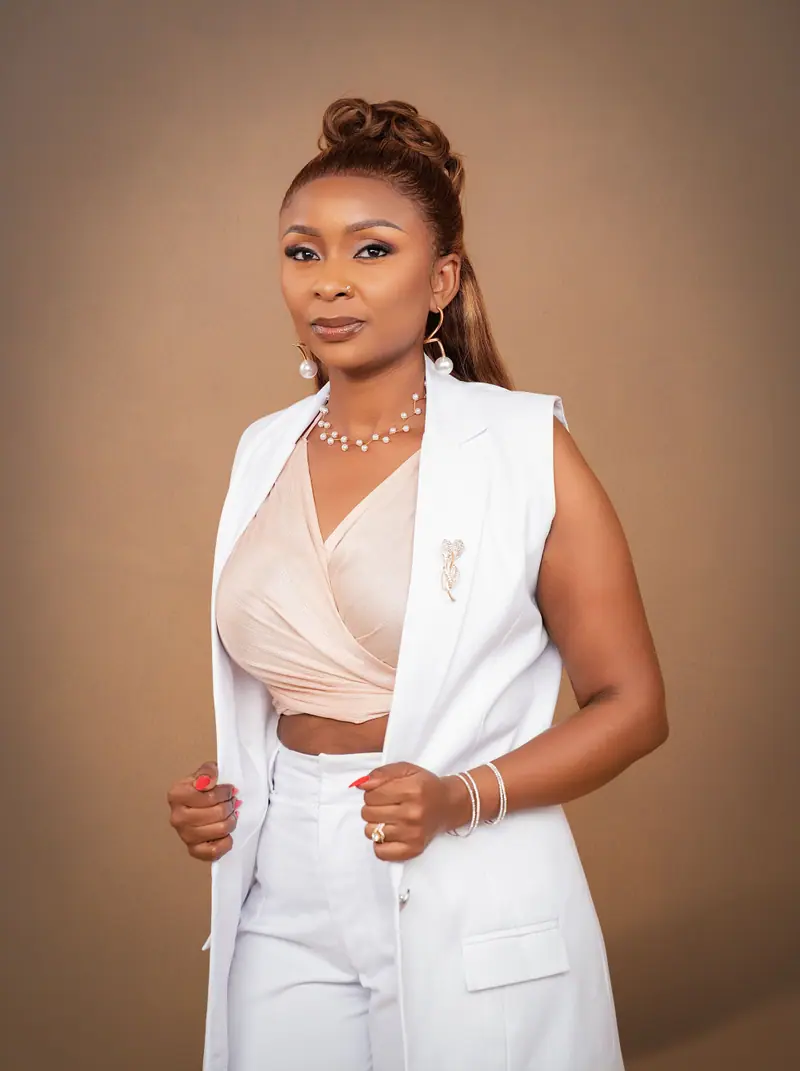 Woman in a white waistcoat and pearl jewellery against a warm tan backdrop