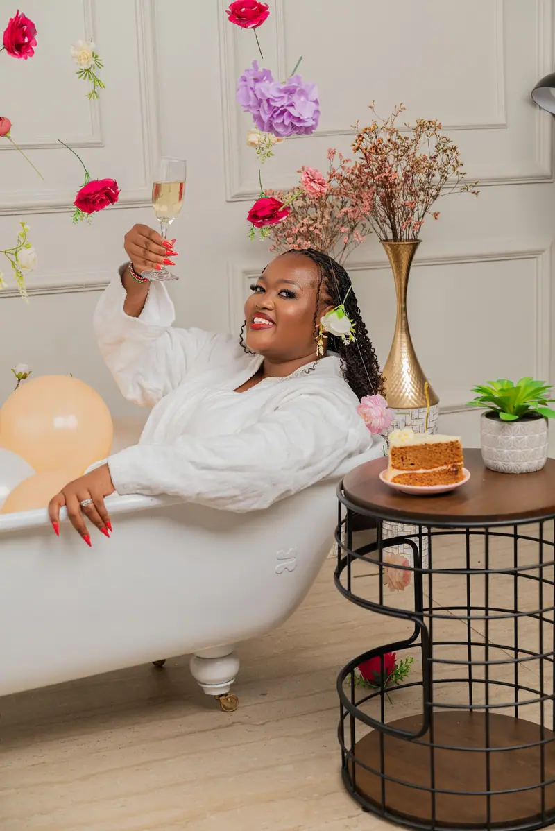 Woman in a white robe lying back in a bathtub with a cake and flowers